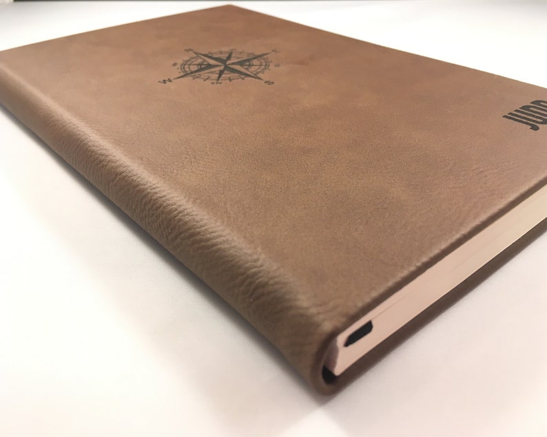 May include: A brown leather-bound journal with a compass design and the word "Journal" embossed on the cover.