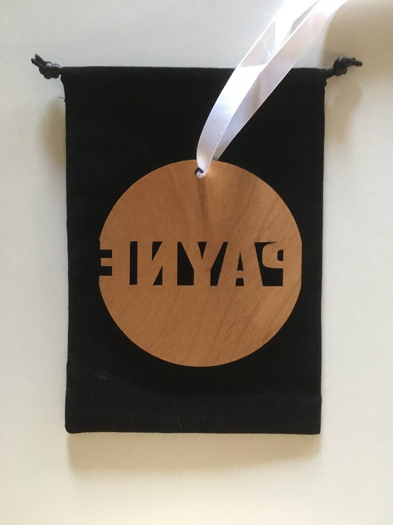 May include: A round wooden ornament with the word "PLAY" cut out in black lettering. The ornament is hanging from a white ribbon and is in a black velvet bag.