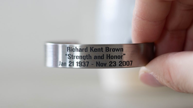 May include: A silver metal bracelet engraved with "Richard Kent Brown" and the inscription "Strength and Honor". The dates "Jan 21 1937 - Nov 23 2007" are also engraved on the bracelet.