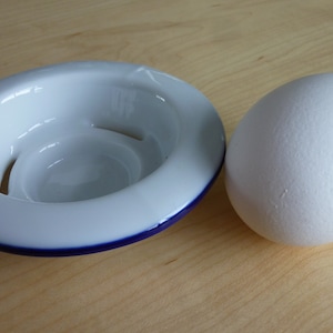 May include: A white ceramic egg cup with a blue rim and a white egg.