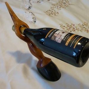 May include: A wooden wine bottle holder shaped like a bird's head with a bottle of Dona Carla Douro Premium 2016 wine.