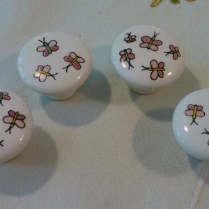 May include: Four white ceramic knobs with pink and green butterfly designs.