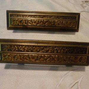 Peut inclure: Deux poignées de tiroir en laiton antique avec une finition martelée texturée et une bordure rectangulaire surélevée.