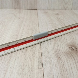 May include: A white and red architectural scale ruler with millimeter and centimetre markings. The ruler has a grey plastic handle and is designed for precise measurements. The scale is marked from 0 to 200 mm.