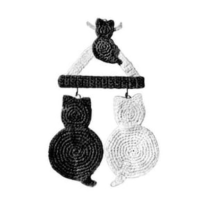 Op de afbeelding: Een gehaakte kattenmobiel met drie zwarte en witte katten die aan een driehoekig frame hangen.