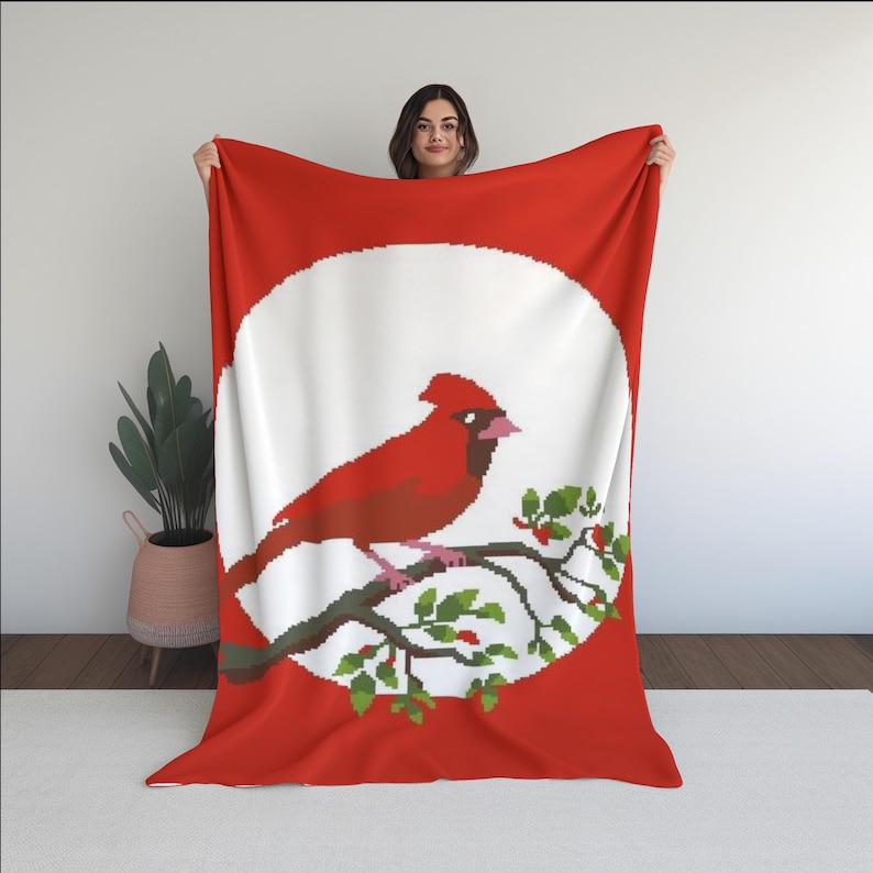 Puede incluir: Un p&aacute;jaro cardenal rojo posado en una rama con hojas verdes y bayas rojas, sobre un c&iacute;rculo blanco sobre un fondo rojo. La imagen est&aacute; en una suave manta de franela roja.