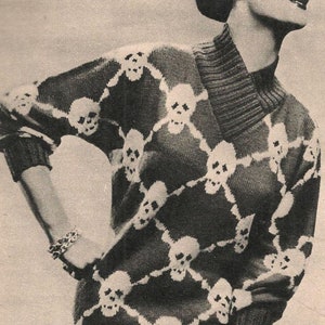 K&ouml;nnte beinhalten: Ein schwarz-wei&szlig;er Strickpullover mit Totenkopf-Muster. Der Pullover hat einen Rollkragen und lange &Auml;rmel.