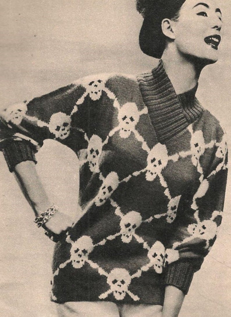 K&ouml;nnte beinhalten: Ein schwarz-wei&szlig;er Strickpullover mit Totenkopf-Muster. Der Pullover hat einen Rollkragen und lange &Auml;rmel.
