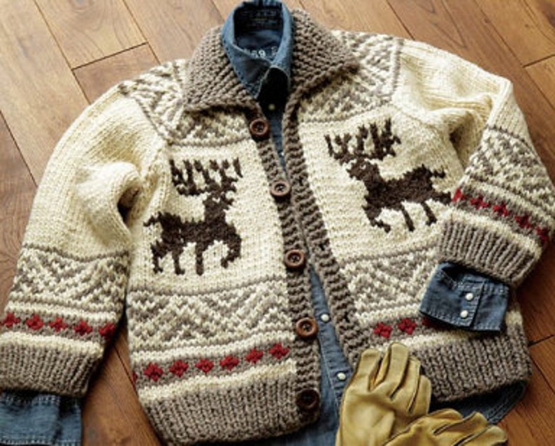 May include: A chunky knit cardigan featuring a cream base with brown reindeer motifs, a large collar, and five dark brown buttons. The sweater displays geometric patterns in brown and red accents along the hem and sleeves, layered over a blue denim shirt.