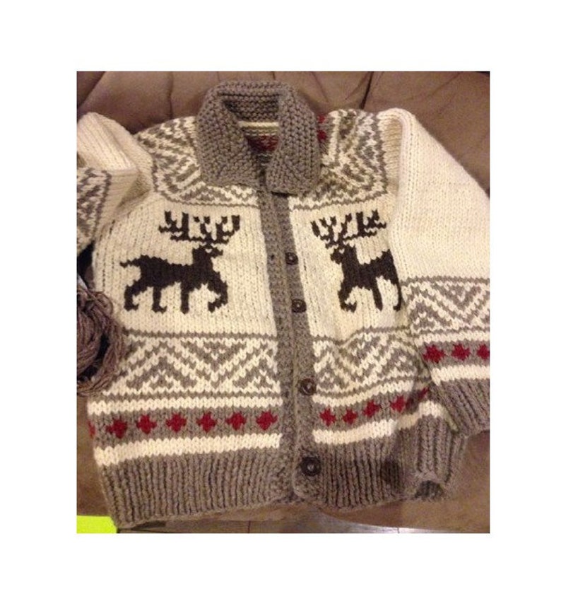 May include: A chunky knit cardigan featuring a cream-colored base with dark brown reindeer silhouettes on the chest. The garment includes a grey collar, grey ribbed cuffs and hem, and a geometric pattern in grey and red across the midsection.