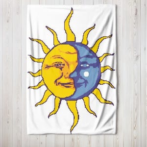 May include: White tapestry featuring a pixelated design of a smiling sun and moon face. The sun is yellow, and the moon is blue, with a white background. The sun has long, yellow rays extending outward.