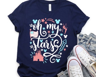 Può includere: Una maglietta blu navy con il testo "Oh my stars" in bianco con accenti rosa e blu. Il design include una bandiera americana rossa, bianca e blu, un castello rosa, stelle, fuochi d'artificio e silhouette di Topolino.