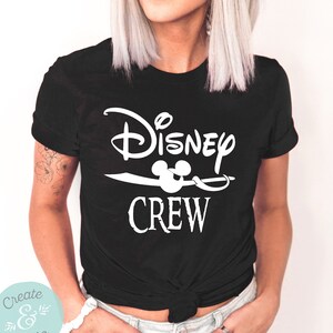 以下が含まれることがあります： 白い文字で「Disney Crew」と書かれた黒いTシャツ。Crewの文字の上にミッキーマウスの頭部のアイコンがあります。