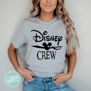 以下が含まれることがあります： 黒い文字で「Disney Crew」と書いてあるグレーのTシャツ。ミッキーマウスの頭部のグラフィックが描かれている。