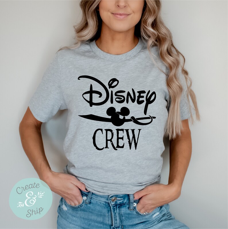 以下が含まれることがあります： 黒い文字で「Disney Crew」と書いてあるグレーのTシャツ。ミッキーマウスの頭部のグラフィックが描かれている。