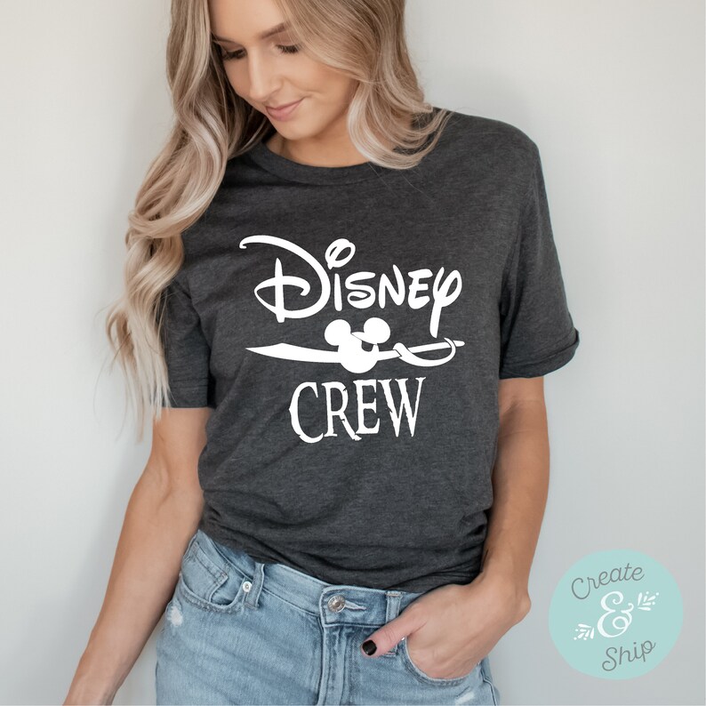 以下が含まれることがあります： 「Disney Crew」と白で書かれたグラフィックデザインが施された濃いグレーのTシャツ。Crewの文字の上にミッキーマウスの頭が描かれている。
