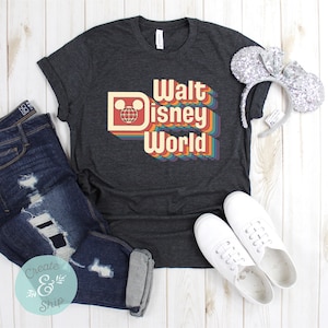Puede incluir: Camiseta gris oscuro con la frase "Walt Disney World" en un dise&ntilde;o retro arco&iacute;ris. La camiseta se combina con vaqueros azules desgastados, zapatillas blancas y orejas de rat&oacute;n con lentejuelas. Un atuendo informal.