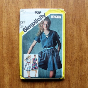 May include: A Simplicity 5583 sewing pattern envelope featuring an Esprit design. The cover displays a photograph of a person wearing a dark blue short-sleeved dress with a light blue belt, alongside smaller images of striped and floral dress variations.