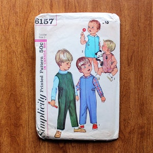 May include: A Simplicity sewing pattern envelope, number 6157, for toddler size 1 clothing. The white paper envelope features illustrations of children wearing various styles of overalls and jumpsuits in blue, green, and plaid patterns.