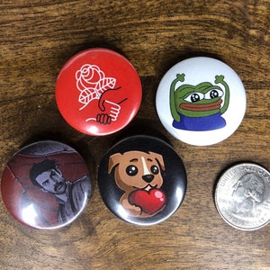 May include: Four round button pins with different designs. One pin features a red background with a white rose and a hand reaching out. Another pin has a white background with a green cartoon frog with blue arms. The third pin has a black background with a brown cartoon puppy holding a red heart. The last pin has a red background with a man with dark hair and a mustache lying down.