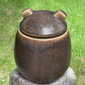 May include: A brown ceramic jar with a lid and two small handles on the lid. The jar has a speckled brown glaze.