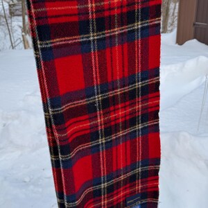 May include: A red, black, and navy plaid scarf with fringed edges. The scarf is hanging outside in the snow. The scarf has a tag that reads "Pendleton".