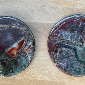 May include: Two round ceramic plates with a brown, white, and green glaze. The plates have a raised design on the surface.