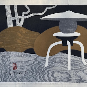 May include: A black and white woodblock print of a Japanese garden scene. The print features a stone lantern with a white roof and a brown rock in the background. The print is signed by the artist, "Kogure Naoto".