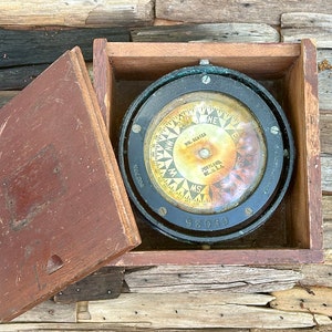 May include: A vintage compass in a wooden box. The compass face is black with a gold needle and markings. The compass is labeled "W.R. Senter, Portland, Me. U.S.A." and "52035".