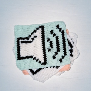 Puede incluir: Un conjunto de tres cuadrados de crochet, cada uno con un color y un diseño diferentes. El cuadrado superior es verde claro con un contorno negro de un icono de altavoz. El cuadrado del medio es blanco con un contorno negro de un icono de altavoz. El cuadrado inferior es melocotón con un contorno negro de un icono de altavoz.