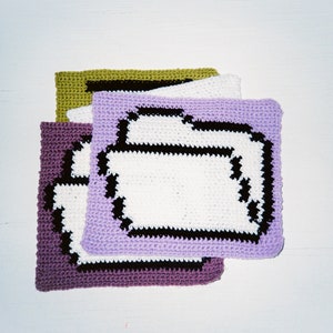 Puede incluir: Tres cuadrados de crochet, uno morado, uno blanco con ribete negro y uno verde, están apilados uno encima del otro. El cuadrado blanco tiene un contorno negro en forma de carpeta.