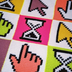 Könnte beinhalten: Eine gehäkelte Decke mit einem pixeligen Design, das verschiedene Computersymbole zeigt, darunter eine Sanduhr, einen Cursor und einen Handzeiger. Die Decke ist aus buntem Garn in den Farben Rosa, Grün, Gelb, Orange und Lila gefertigt.
