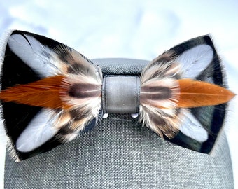 May include: A bow tie made of brown, white, and black feathers. The bow tie is tied with a gray ribbon.
