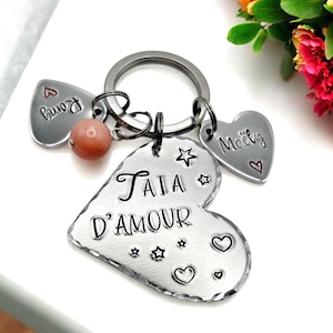 Może przedstawiać: Srebrny brelok w kształcie serca z wygrawerowanym napisem "Tata d'Amour". Brelok ma również dwa mniejsze charmsy w kształcie serca z wygrawerowanymi napisami "Mommy" i "Papa".