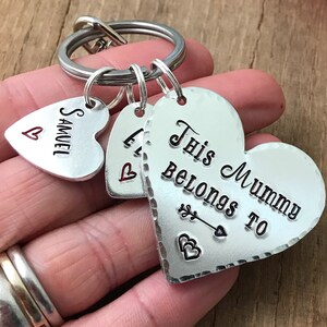 May include: Silver heart-shaped keychain with the text "This Mummy Belongs To" and a small arrow with two hearts. There are two smaller heart-shaped charms with the text "Samuel" and "L" on them.