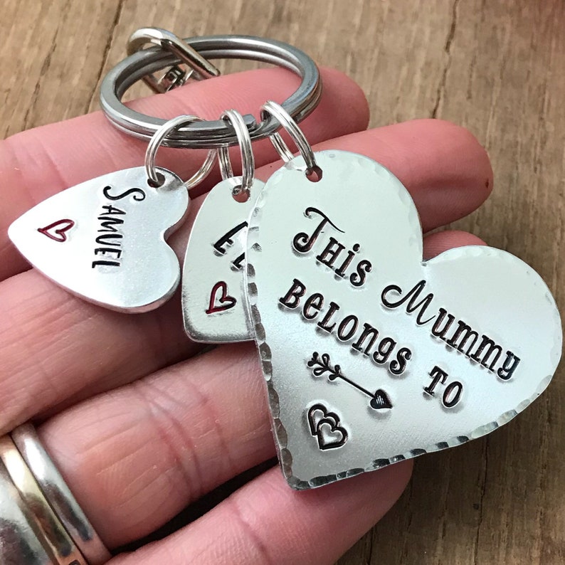 May include: Silver heart-shaped keychain with the text "This Mummy Belongs To" and a small arrow with two hearts. There are two smaller heart-shaped charms with the text "Samuel" and "L" on them.