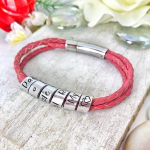 Könnte beinhalten: Rosa Lederarmband mit silbernen Perlen, auf denen "Dad", "Cole", "Riley", "My" und ein Herz stehen.