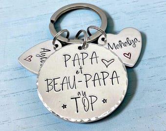 May include: A silver-toned metal keychain featuring a large circular disc engraved with the text PAPA et BEAU-PAPA au TOP and two smaller heart-shaped charms engraved with the names Ayla and Mahalya, each accented with a small red heart.
