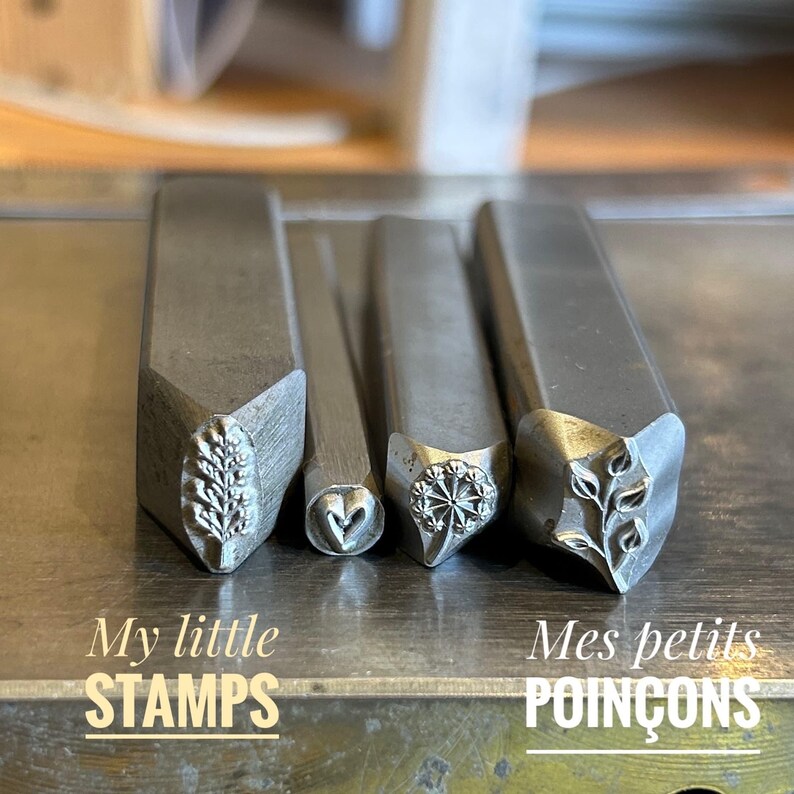 May include: Four metal stamps with different designs: a leafy branch, a heart, a flower, and a vine. The stamps are arranged in a row on a metal surface. The text "My little STAMPS" is below the stamps.