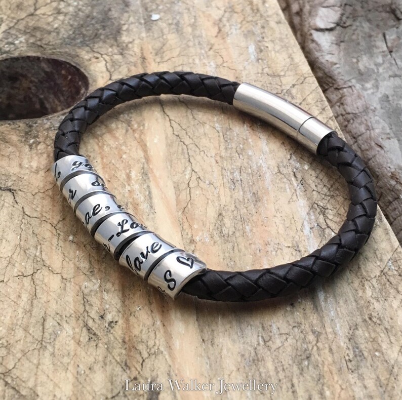 May include: A brown leather bracelet with a silver clasp and multiple silver beads. Each bead has a word engraved on it, including "Love", "Always", and "Kiss".