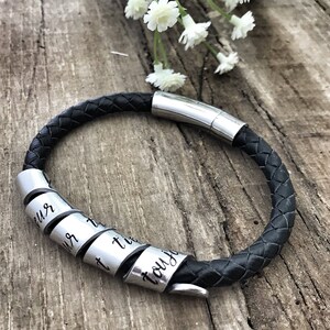 May include: Black leather bracelet with a silver clasp and a silver band with the words "you just" engraved on it.