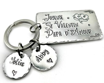 May include: Silver keyring with a rectangular tag that reads "Joyeuse St Valentin Papa d'Amour" with two hearts and stars. There are two smaller round tags with the names "Yolene" and "Alby" on them.
