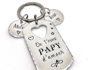 May include: A silver-toned metal keyring featuring a large rectangular tag with a heart-shaped cutout, engraved with the text On t'aime PAPY d'amour, stars, and a heart. Two smaller circular tags are attached, engraved with the names Mali and Aria.