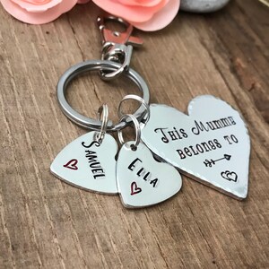 May include: Silver heart-shaped keychain with the text "This Mummy Belongs To" and two smaller heart-shaped charms with the names "Samuel" and "Ella" engraved on them.