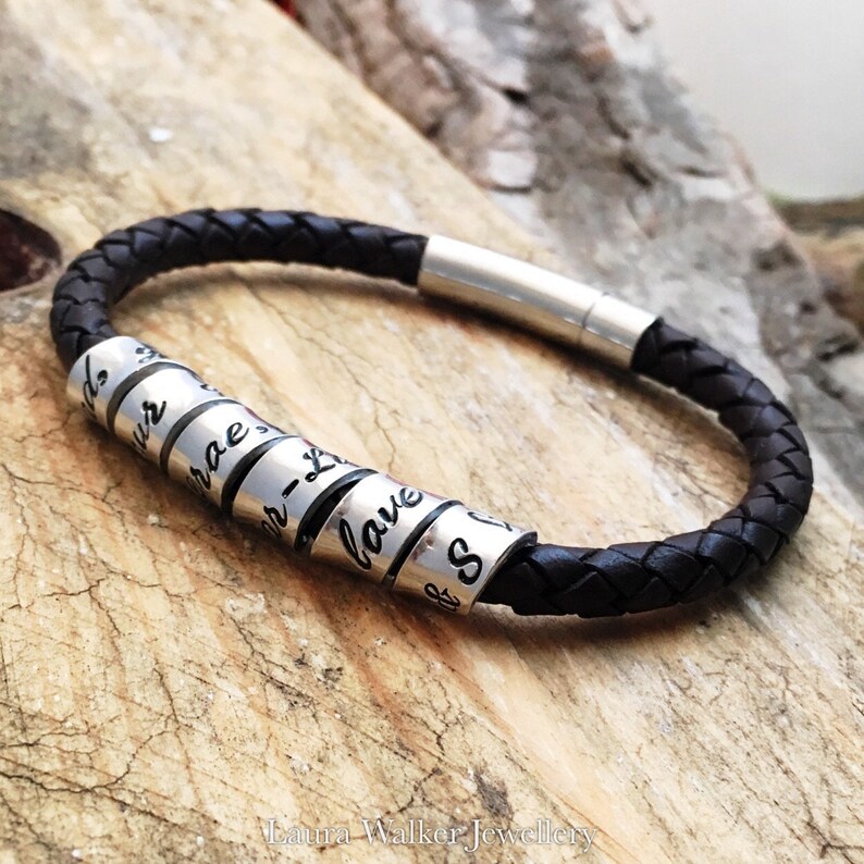 May include: A black leather bracelet with silver beads that have words engraved on them. The words on the beads are "friends", "love", "our", "brave", "always", "and", "so".