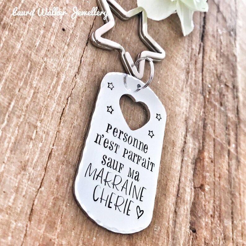 May include: Silver keychain with a heart-shaped cutout and the text "Personne n'est parfait sauf ma marraine ch&eacute;rie" (No one is perfect except my dear godmother).