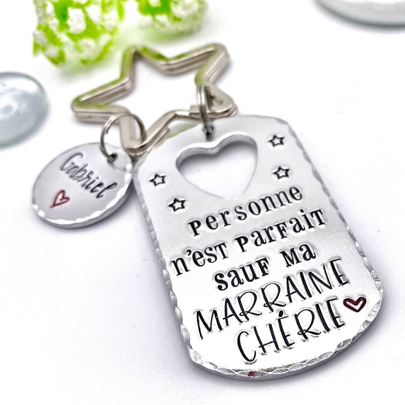 May include: Silver keychain with a star-shaped ring and a tag that says "Personne n'est parfait sauf ma marraine ch&eacute;rie" with a heart cutout and two stars. A smaller silver tag with the name "Gabriel" and a heart is attached to the ring.
