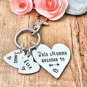 May include: Silver heart-shaped keychain with the text "This Mummy Belongs To" and two smaller heart charms with the names "Samuel" and "Ella" engraved on them.