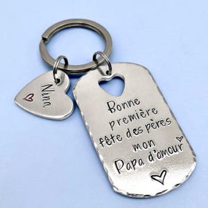 Peut inclure: Un porte-clés en métal argenté composé d'une plaque rectangulaire aux bords martelés avec une découpe en forme de cœur. La plaque est gravée du texte "Bonne première fête des pères mon Papa d'amour" accompagné de petits cœurs.