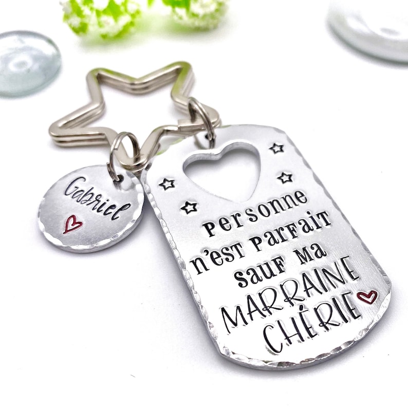May include: Silver keychain with a star-shaped charm and a tag that reads "Personne n'est parfait sauf ma marraine ch&eacute;rie" with a heart. The tag has a heart-shaped cutout and a small charm that says "Gabriel" with a heart.